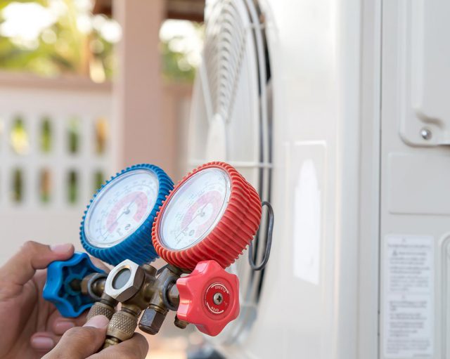 Air repair mechanic using measuring pressure gauge equipment for filling home air conditioner after cleaners and checking maintenance outdoor air compressor unit.