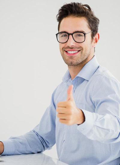 Businessman showing thumbs up while using laptop in office